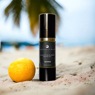 Johnnie Ray Signature Blend Beard Oil in a black airless pump top bottle on a sandy beach with citrus fruit. 