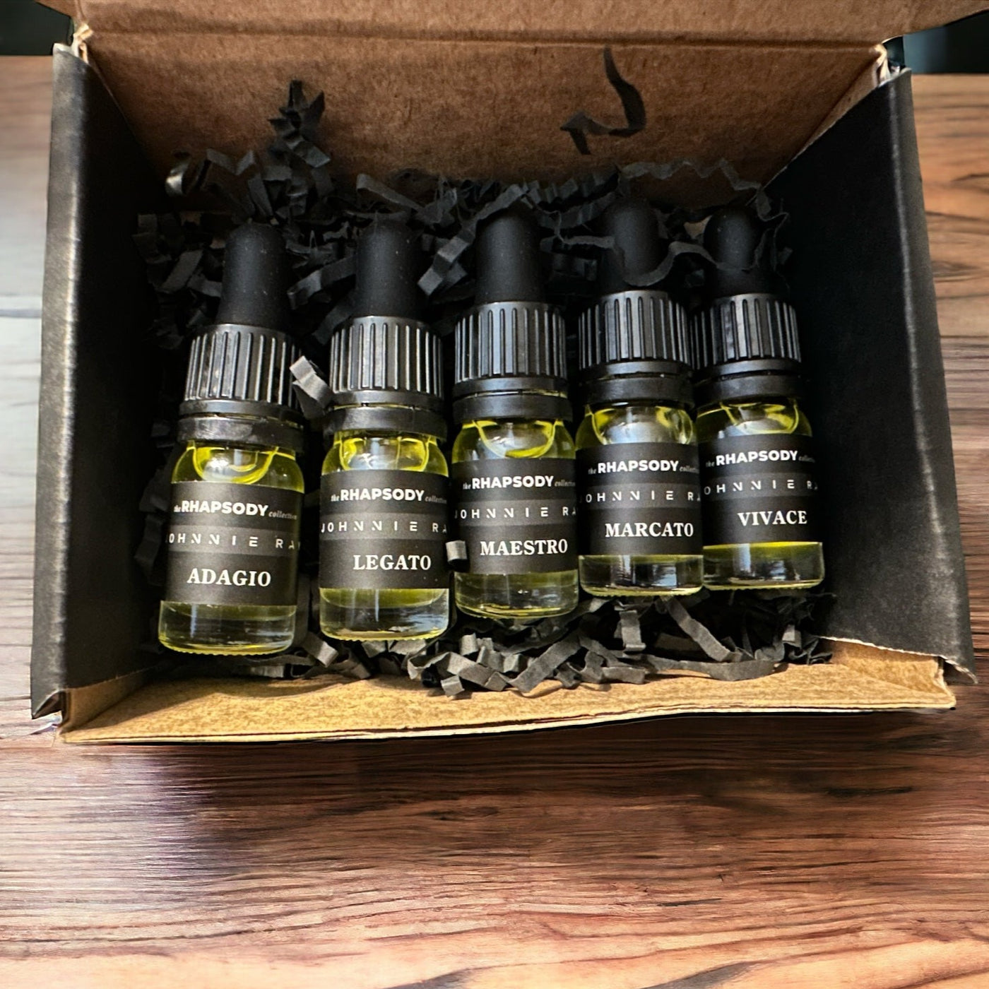 Black box with 5mL bottles of The Rhapsody Collection Signature Blend Beard Oil from Johnnie Ray sitting on a wooden table