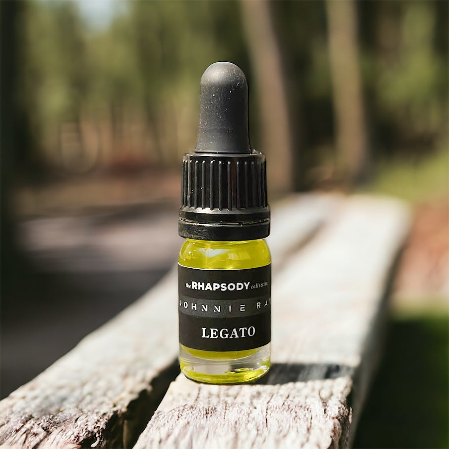 5mL bottle of The Rhapsody Collection Legato Signature Blend Beard Oil from Johnnie Ray sitting on a wood ledge outside