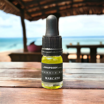 5mL bottle of The Rhapsody Collection Marcato Signature Blend Beard Oil from Johnnie Ray sitting on a wood table by the beach