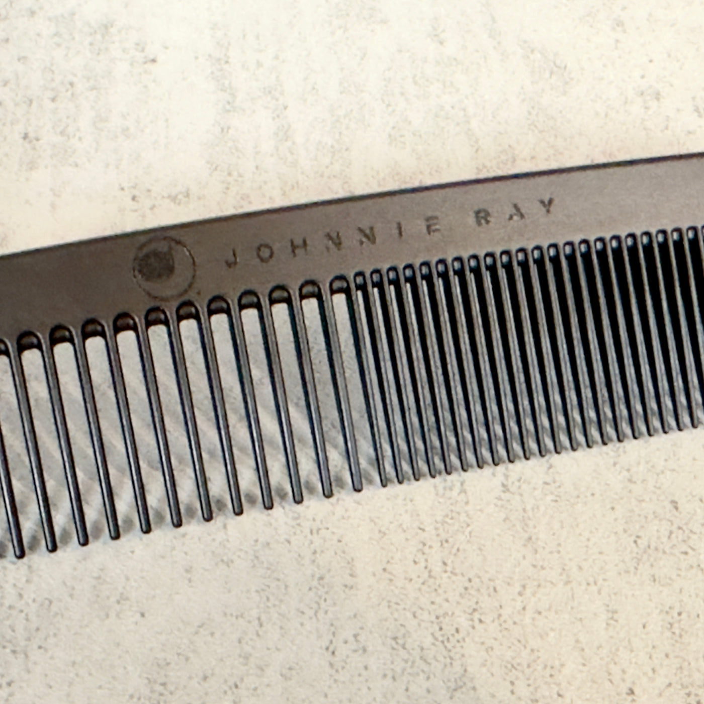 Black Chicago Comb Model 6 angled to show Johnnie Ray logo engraved across the top, laid against a concrete background.