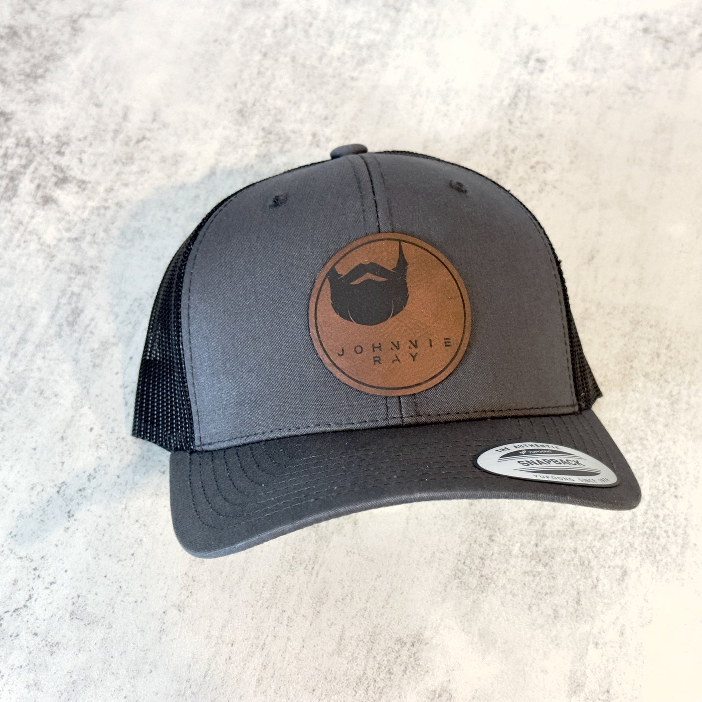 Dark Grey Johnnie Ray hat with round brown leather patch with Johnnie Ray logo.