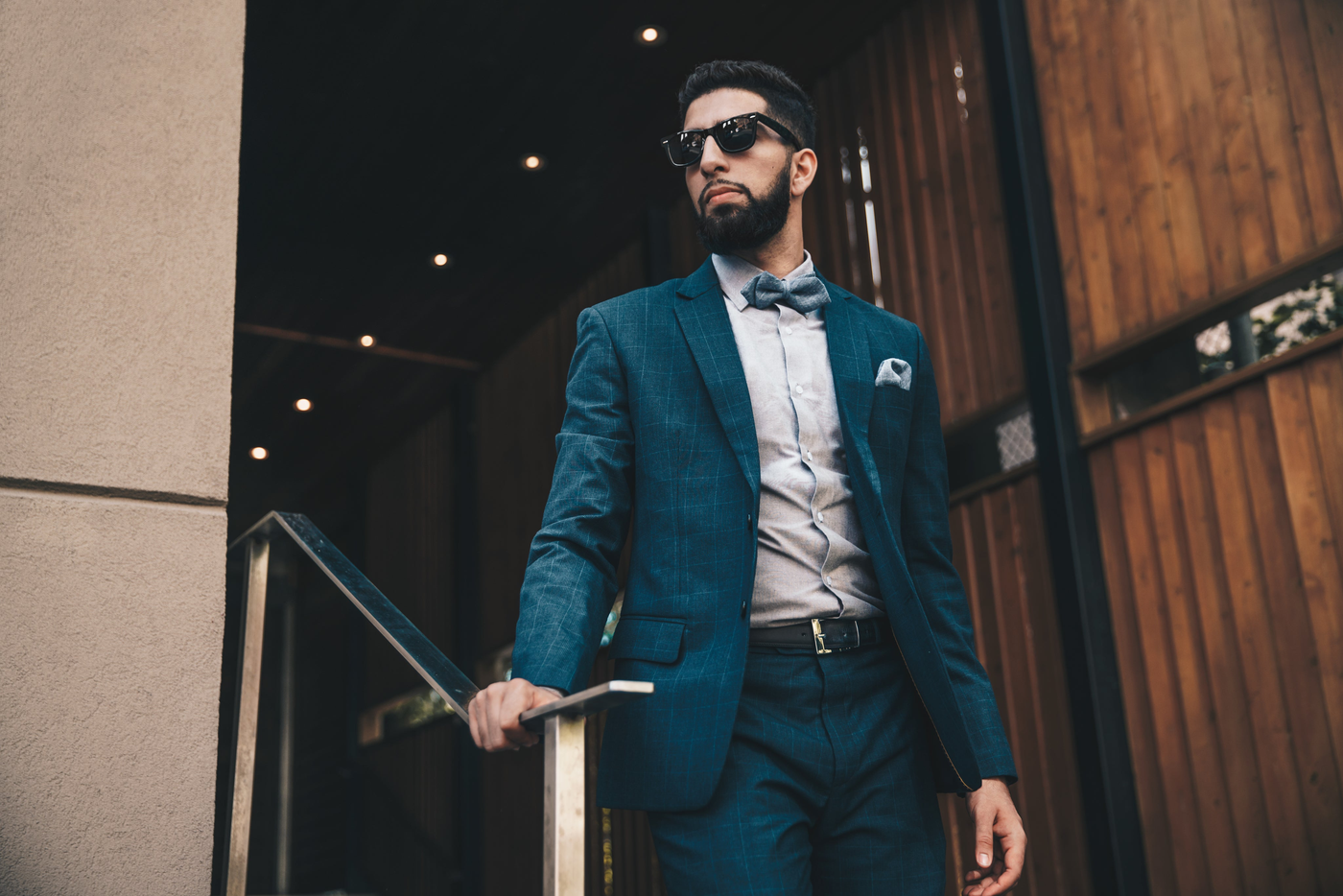 Man with short beard walking down stairs wearing a suit with bowtie and sunglasses.