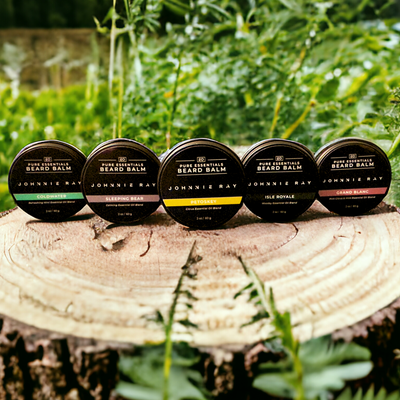 5 tins of Johnnie Ray Pure Essentials Beard Balm on tree stump in grassy area