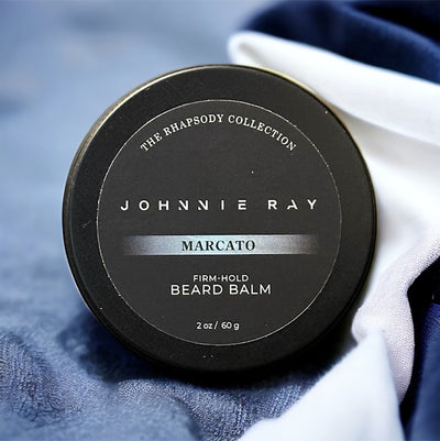 Johnnie Ray Marcato Beard Balm from The Rhapsody Collection in a black tin displayed on blue textured fabric