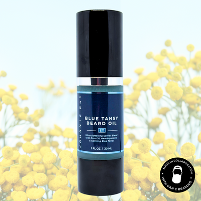 Bottle of Johnnie Ray Blue Tansy Beard Oil with a black cap against blue tansy flowers