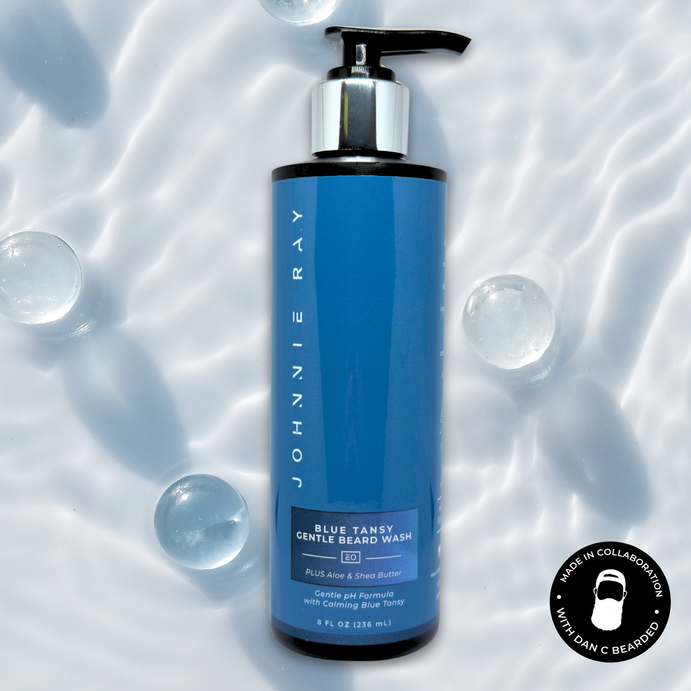 Black bottle of Johnnie Ray Blue Tansy Beard Wash with a blue label against a water background with bubbles