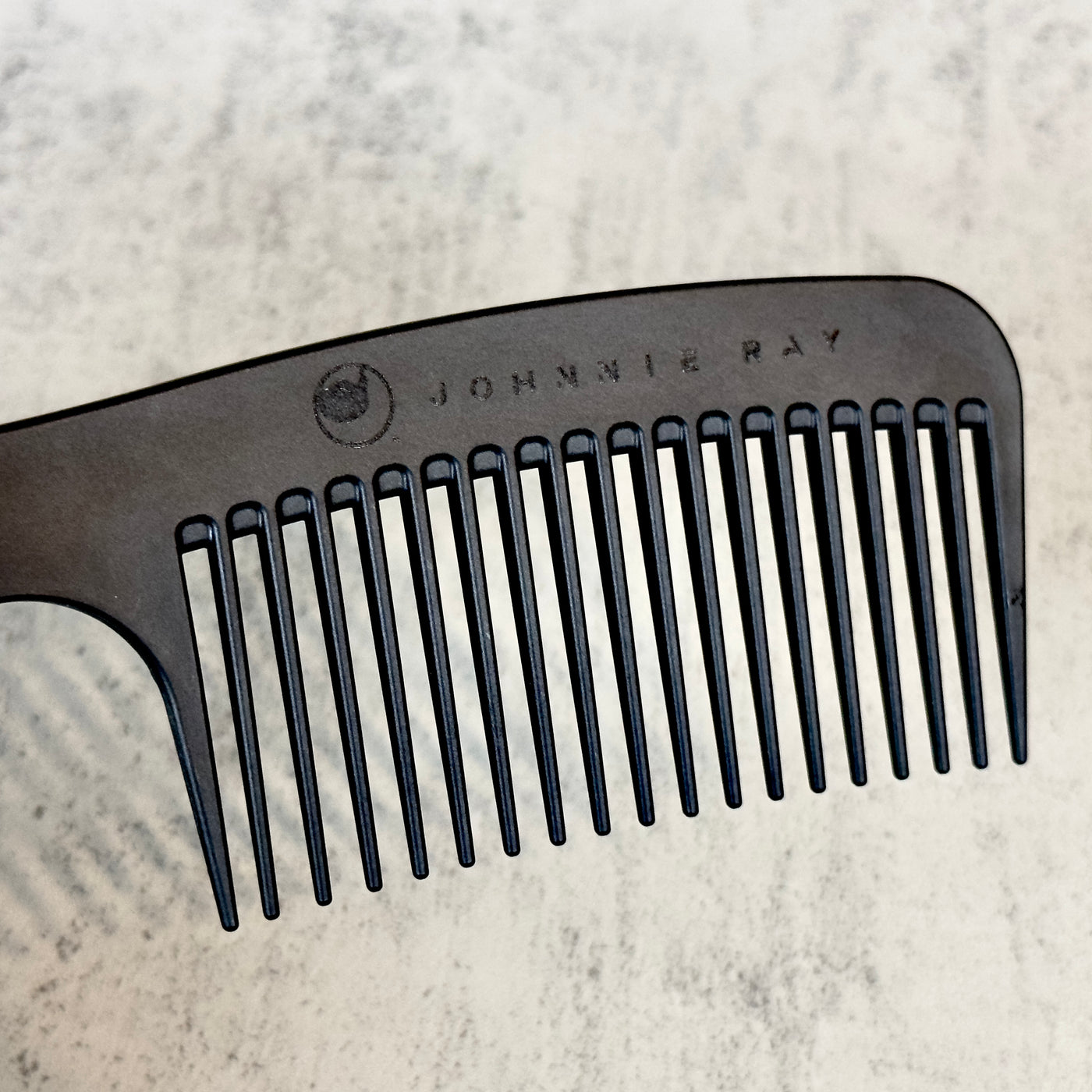 Black Chicago Comb Model 8 laid at an angle to show Johnnie Ray logo engraving across the top against concrete background.