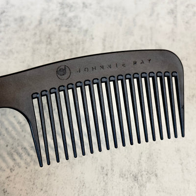 Black Chicago Comb Model 8 laid at an angle to show Johnnie Ray logo engraving across the top against concrete background.