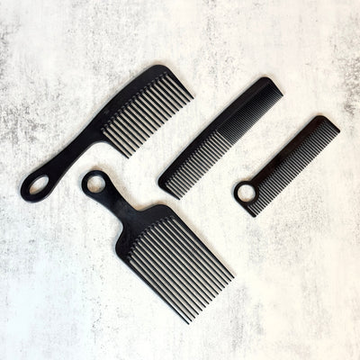 4 black Johnnie Ray engraved Chicago Comb beard combs arranged against a concrete background.